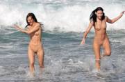 Happy naked girls running away from the crashing waves