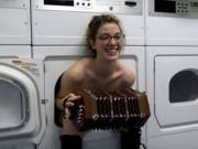 Accordion-wielding topless woman sitting in a washing machine
