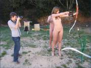 Zita shooting a bow and arrow, naked.