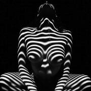 Nude girl in darkness with light making trippy striped pattern on her body