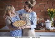 Mother embraces her daughter and guides her hand to show her the right way to display her moist pie