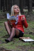 A beautiful Polish girl dressed up and reading about the USA National Parks while sitting in a forest and enjoying a cup of Nescafe and some chocolates