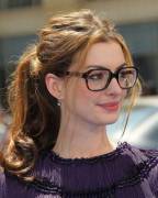 Anne Hathaway with glasses and a loose, messy ponytail