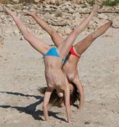 2 girls in bikini bottoms doing hand stands with legs apart